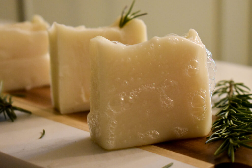 3 bars of white soap on wooden board surrounded by rosemary