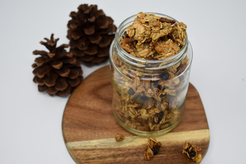 granola in jar on wooden plate with pinecones behind it
