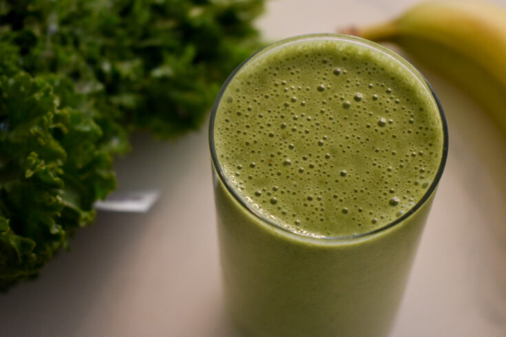 top view of green smoothie next to banana and kale bunch