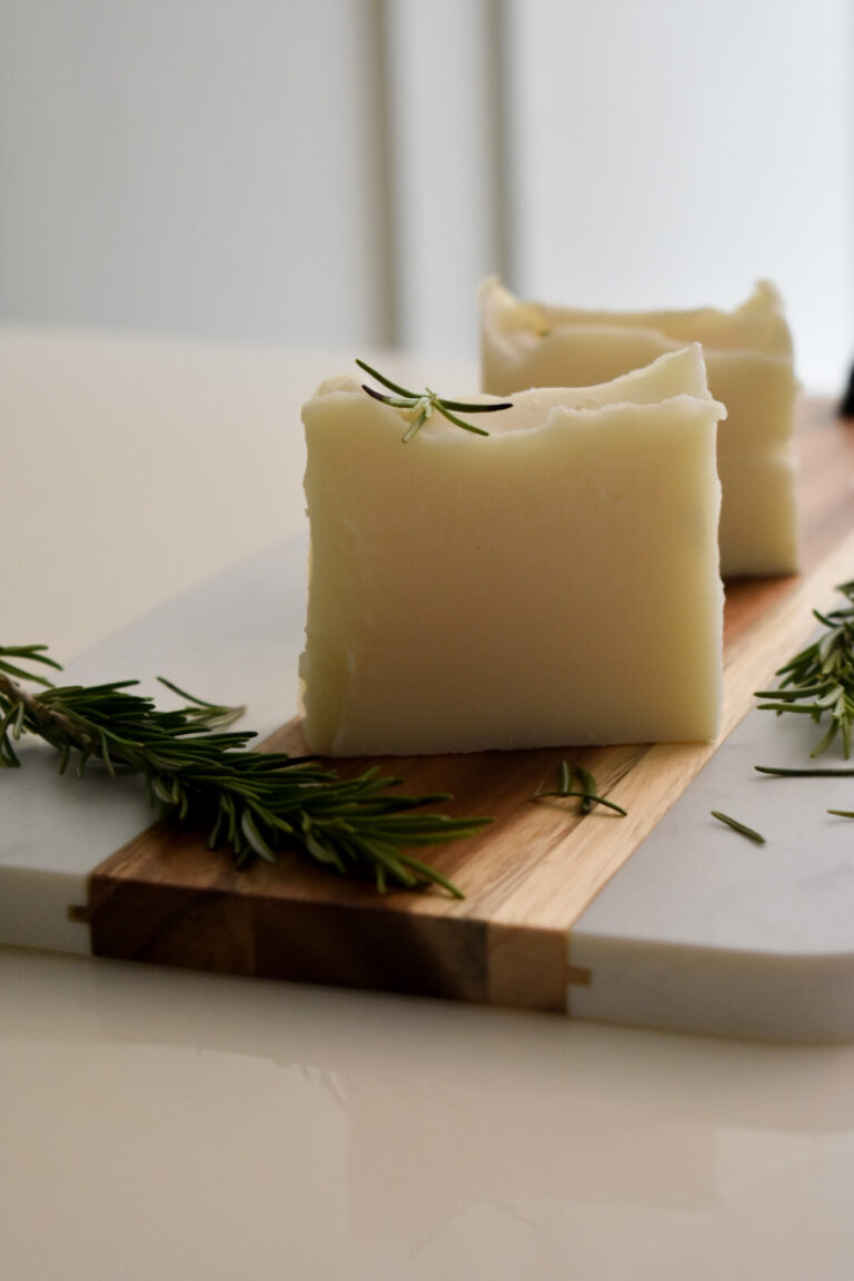 2 bars of white soap on wooden board surrounded by rosemary