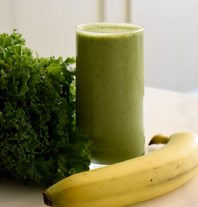 green smoothie next to banana and bunch of kale