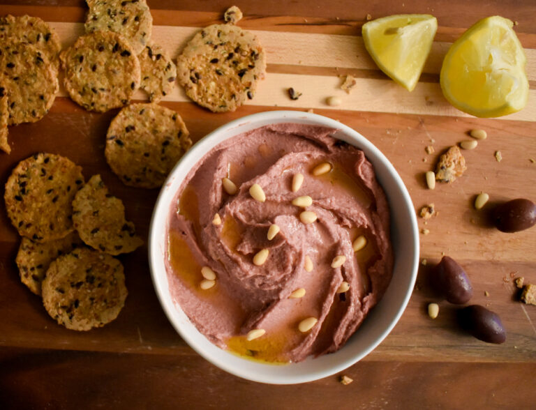 hummus in bowl surrounded by crackers and lemon wedges on wooden board